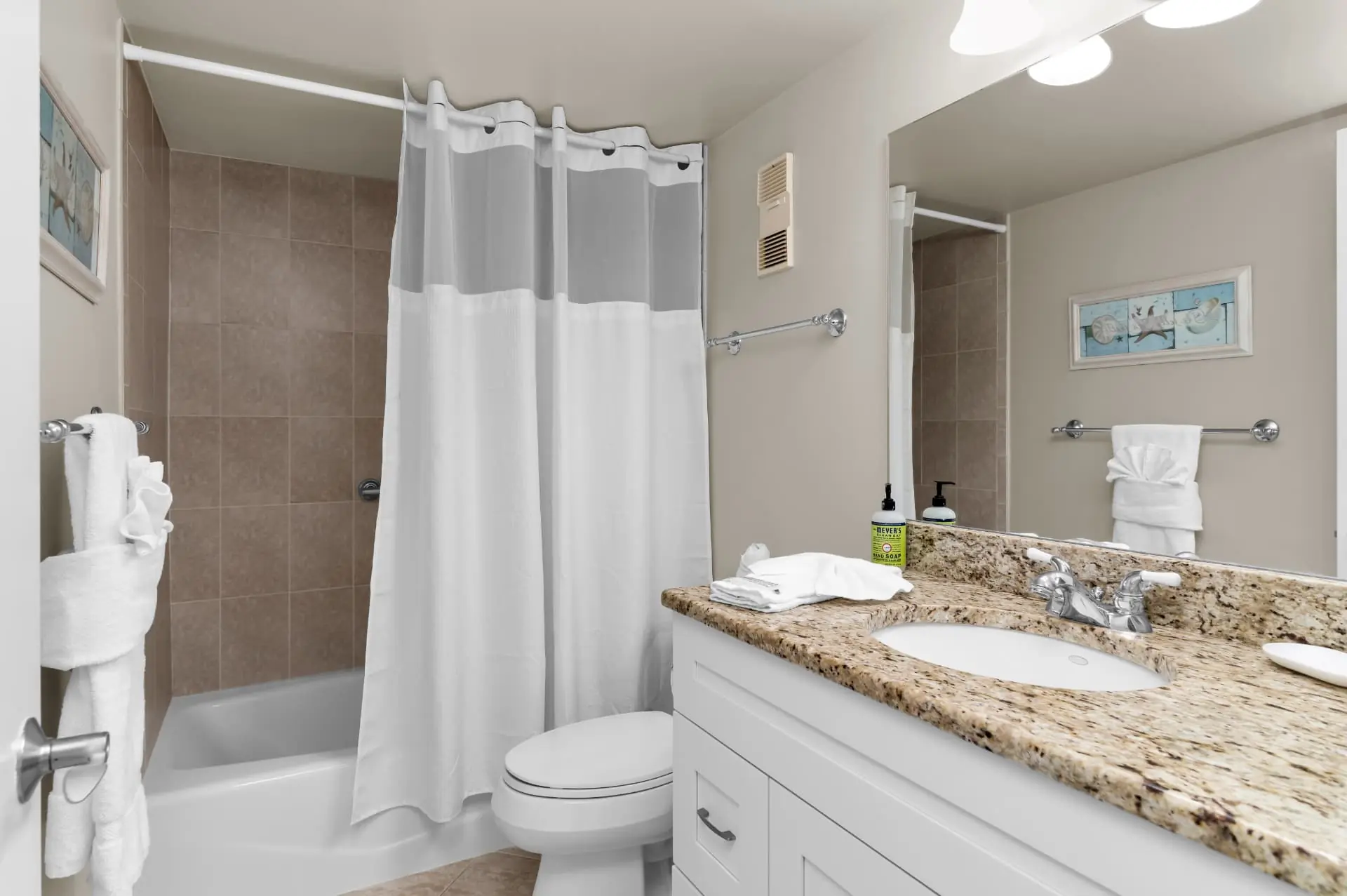 Second bathroom with a granite vanity, coastal artwork and a shower-tub combination