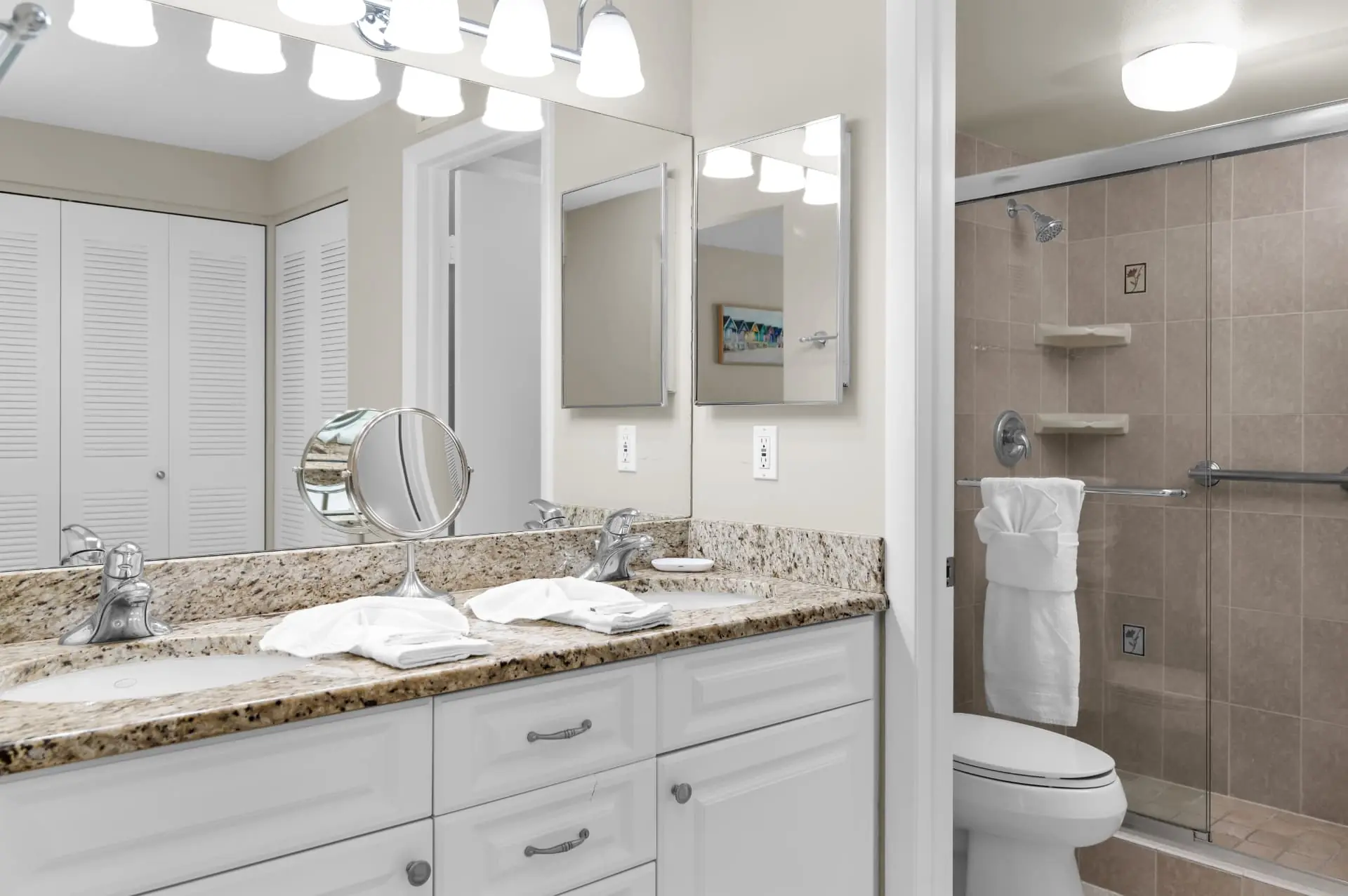 Primary bathroom with a double granite vanity, large mirror and a walk-in shower with glass doors